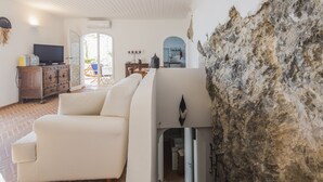 A living room with a white sofa, a television on a wooden cabinet, and a stone wall. - Holidayhome I Delfini Positano (Positano)