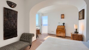 A bedroom with a bed, a chair, a dresser, and a wall with a decorative piece. - Holidayhome I Delfini Positano (Positano)