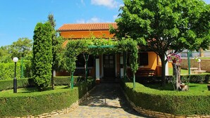 A building with a tiled roof, a paved entrance, and a well-maintained garden with hedges and trees.