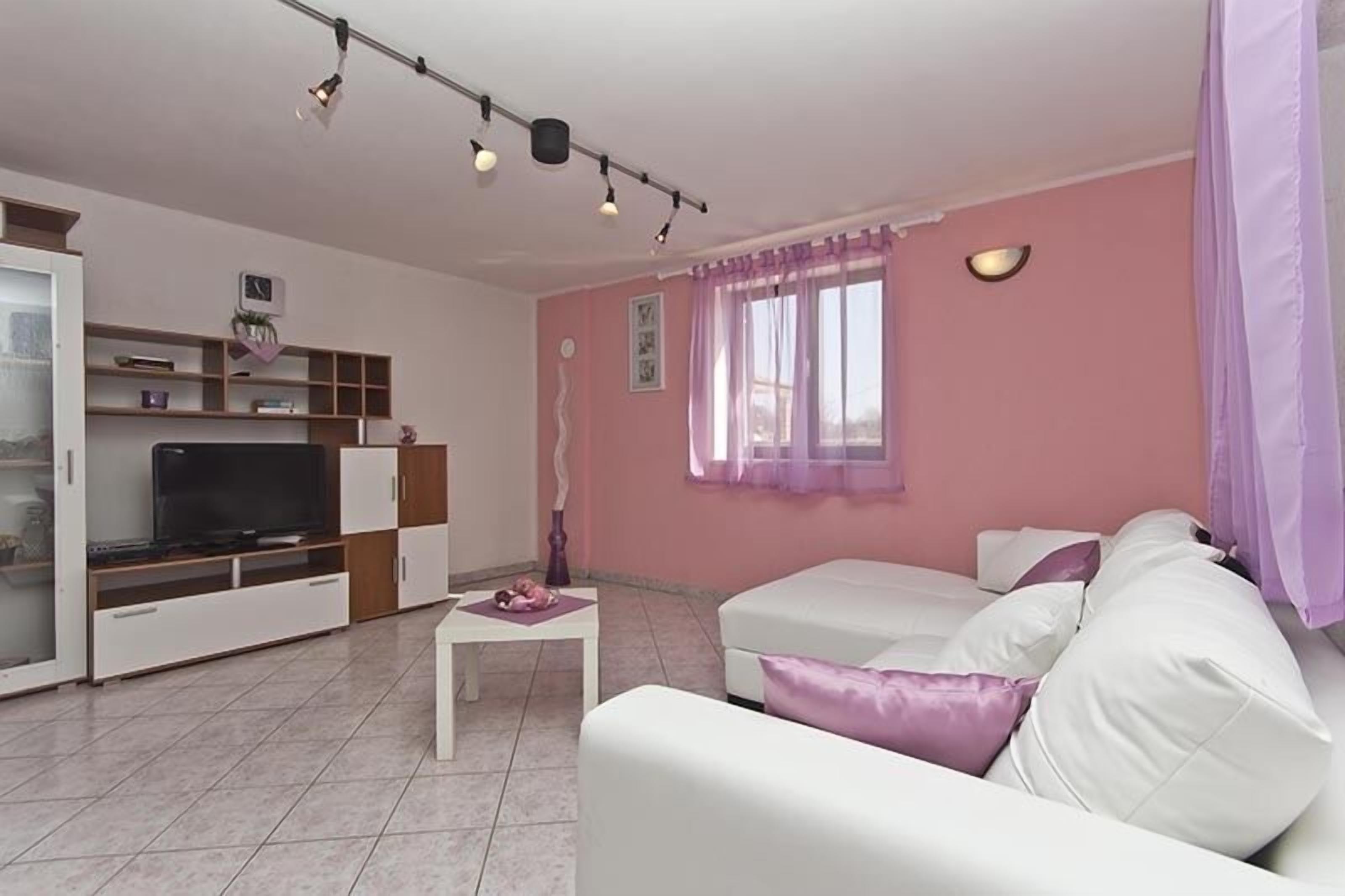 Ein Wohnzimmer mit einem weißen Sofa, einem Fernseher und einem kleinen Tisch.