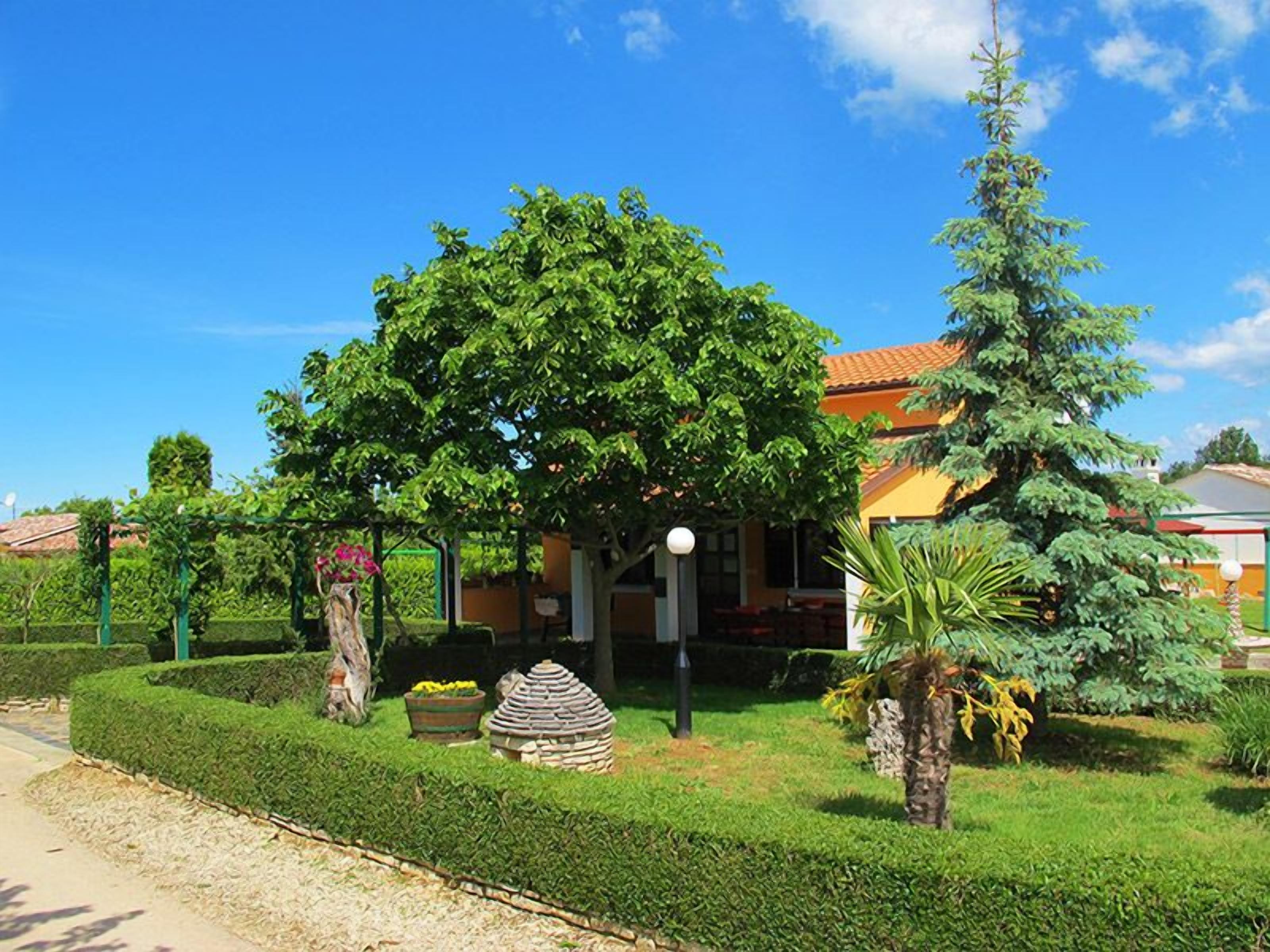 A well-maintained garden with a variety of trees and shrubs, a stone structure, and a building with a red roof.