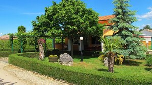 A well-maintained garden with a variety of trees and shrubs, a stone structure, and a building with a red roof.