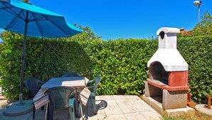 An outdoor patio with a table and chairs, a barbecue grill, and a blue umbrella. - Apartment 534/1277 (Istria - Stinjan), 500m from the beach (Stinjan)