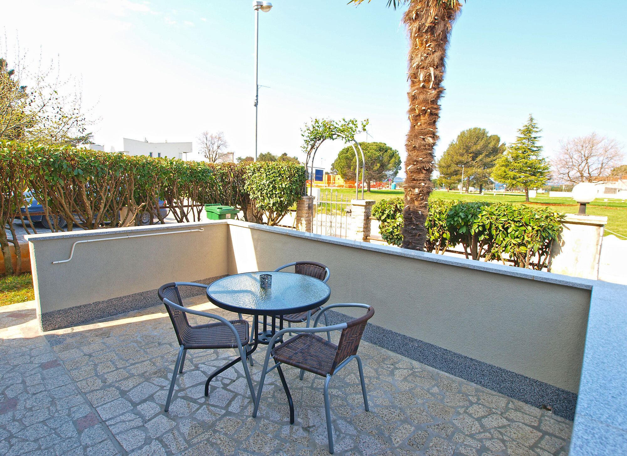 Eine Terrasse im Freien mit einem runden Tisch und vier Stühlen, umgeben von einer niedrigen Mauer und verschiedenen Pflanzen.