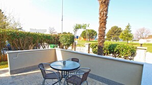 An outdoor patio with a round table and four chairs, surrounded by a low wall and various plants.
