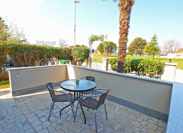 An outdoor patio with a round table and four chairs, surrounded by a low wall and various plants.
