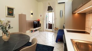 A compact living space with a dining table, a TV, a kitchenette, and a view through a glass door.