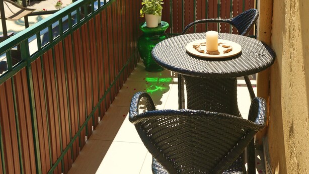 A balcony with a round table, two chairs, a candle, a potted plant, and a palm tree.
