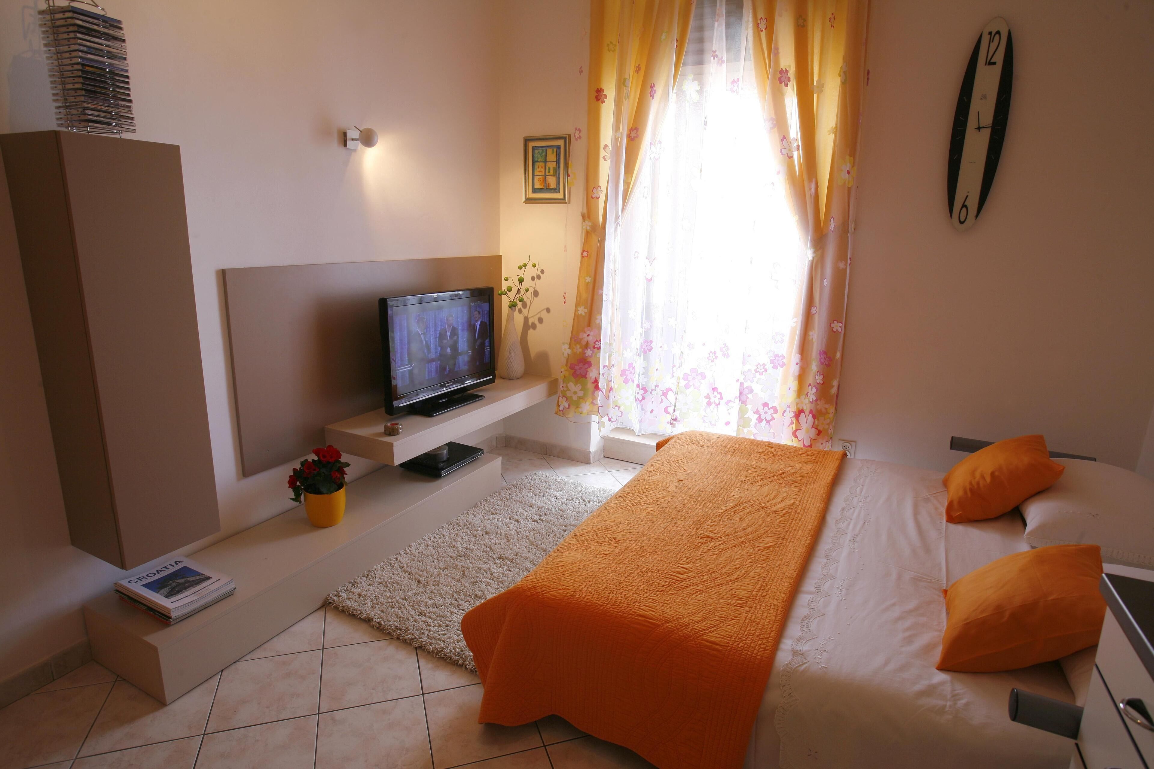 A bedroom with a bed, a television, a small table, and a window with curtains.