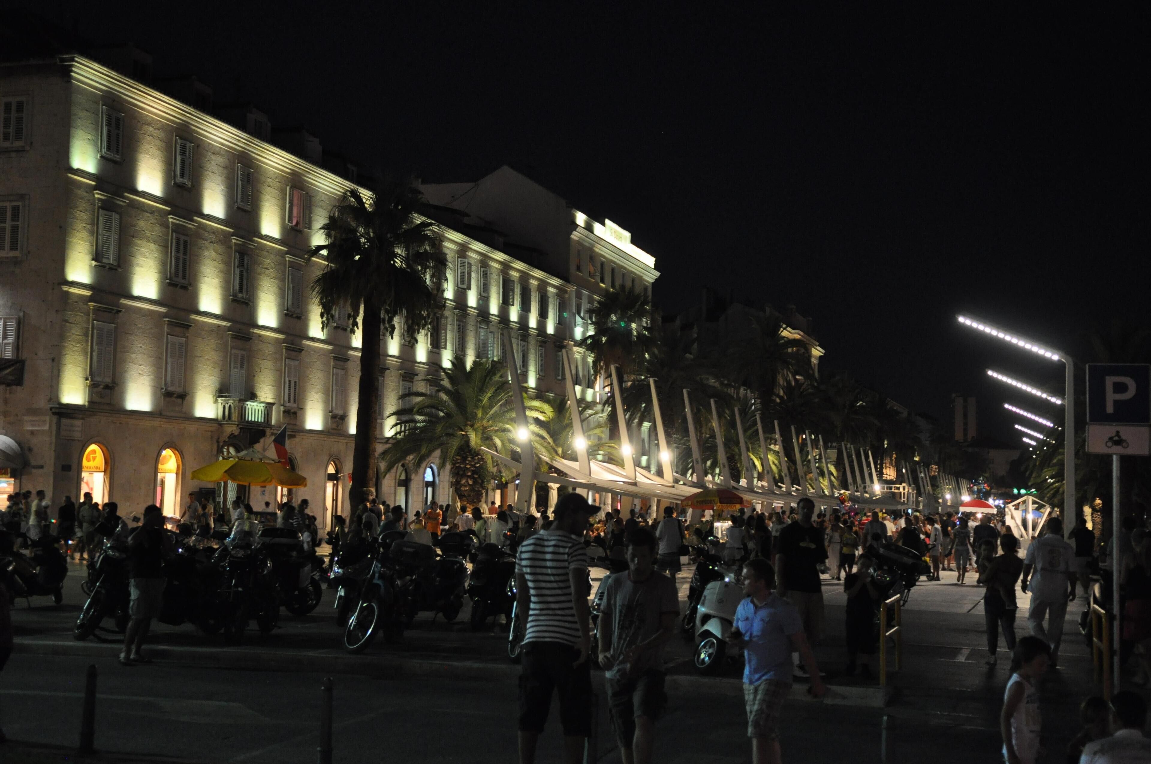 A busy street at night with illuminated buildings and palm trees.