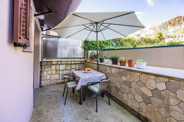 An outdoor patio with a table and chairs, an umbrella, a grill, and potted plants.