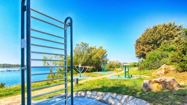 A metal gate leading to a park with exercise equipment and a stone pathway.
