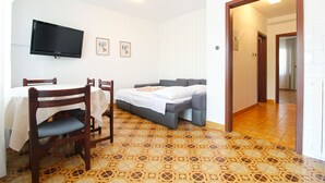 A room with a bed, a table with chairs, a TV mounted on the wall, and a patterned floor.