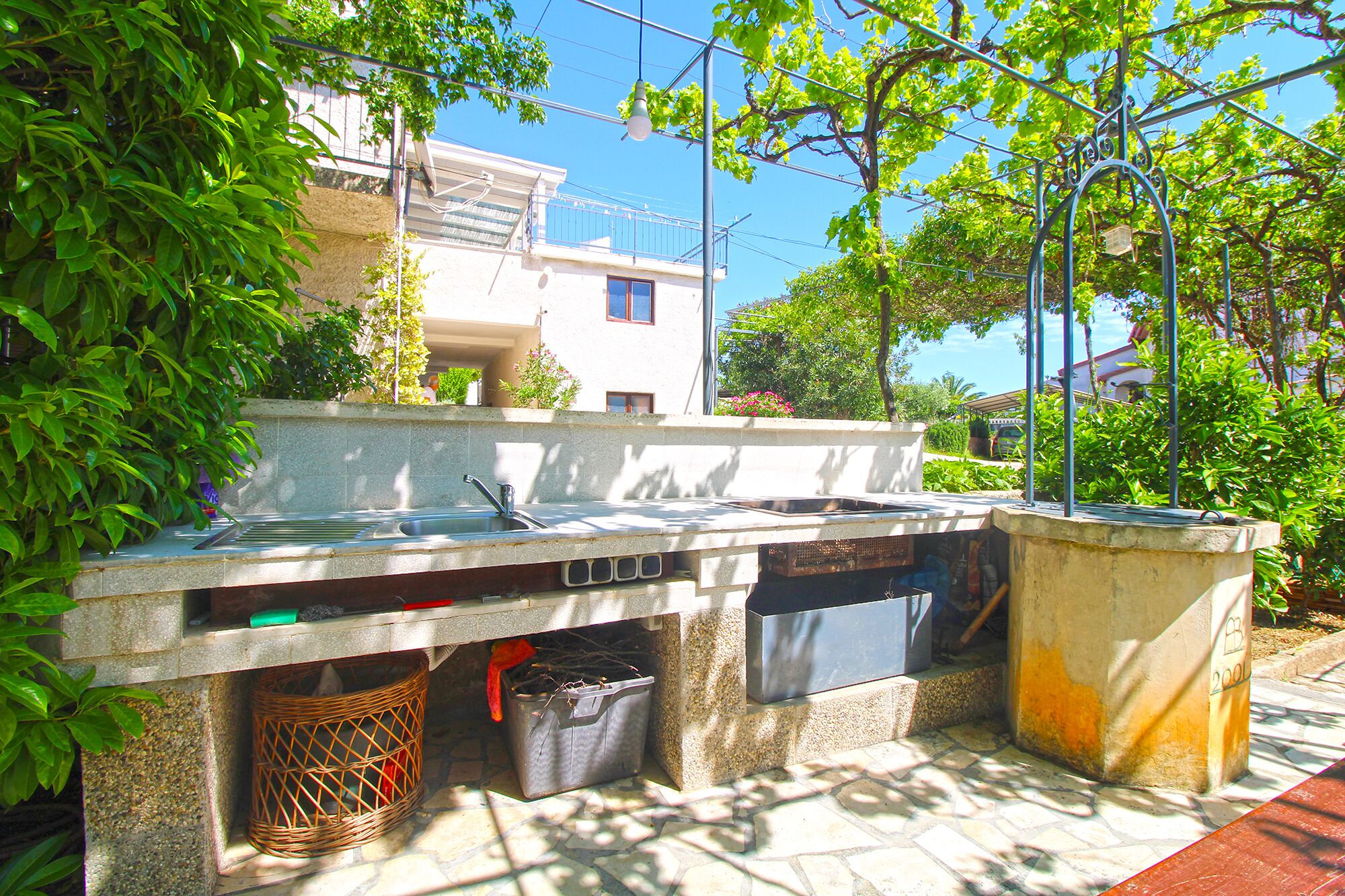 An outdoor kitchen area with a sink, a trash bin, and a planter.
