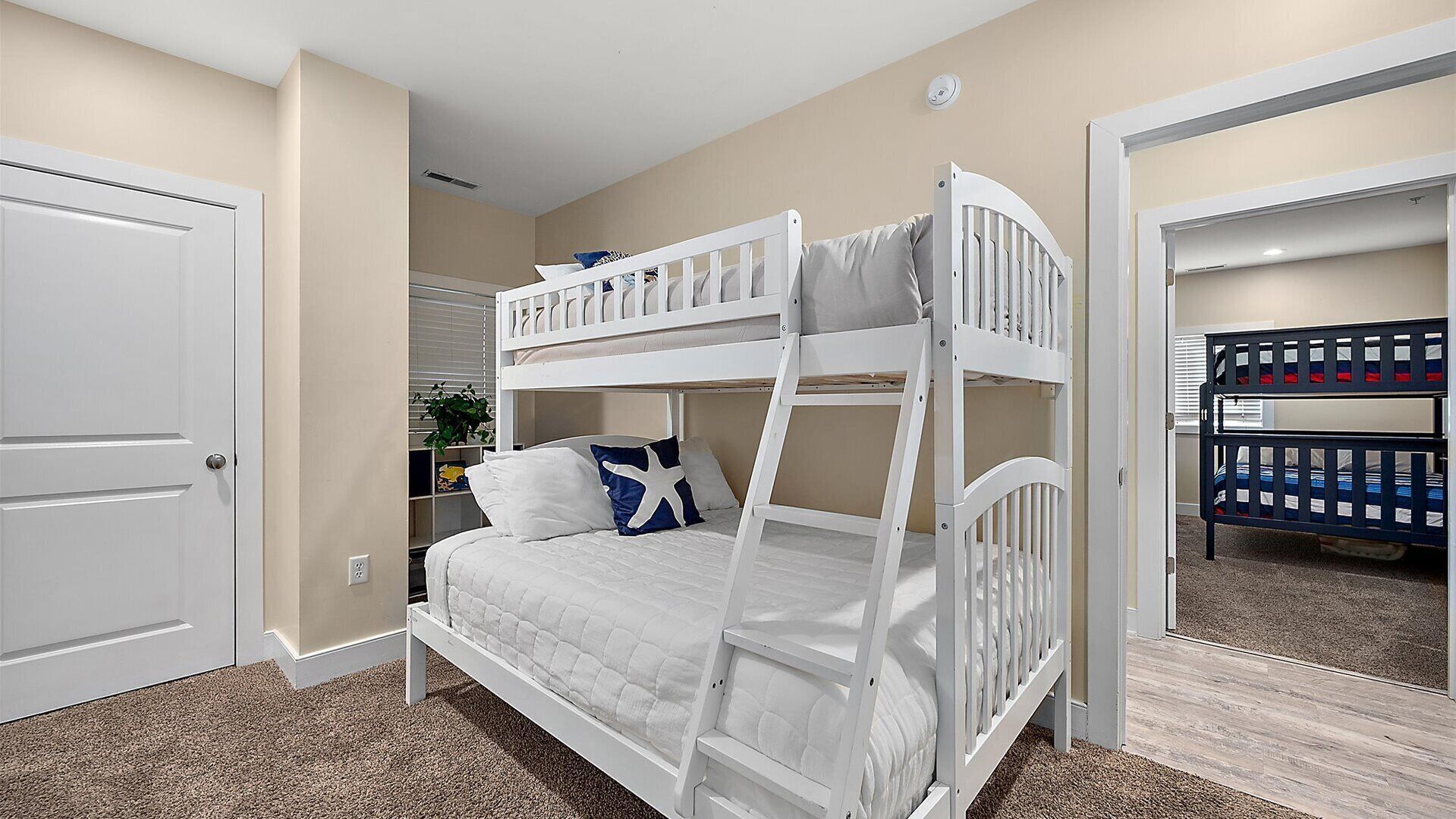 A bunk bed room with a white door, beige walls, and a small plant.