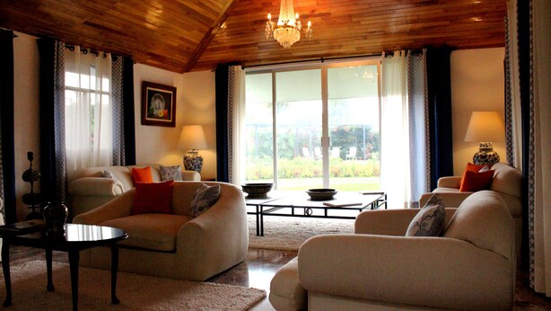 Un soggiorno spazioso con soffitto alto, travi in legno e un'ampia finestra che offre vista sull'esterno. Si notano due divani, un tavolino da caffè e un lampadario.