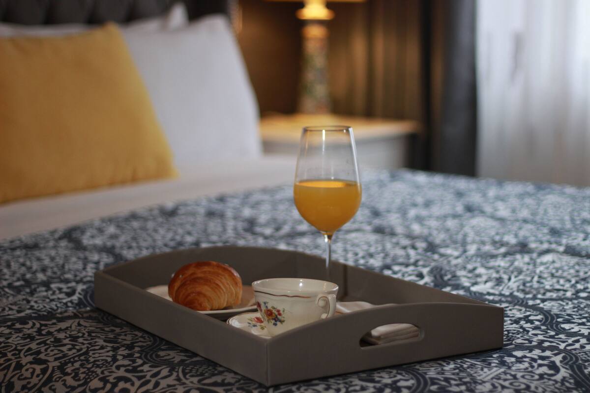 A breakfast tray with croissant and orange juice on a patterned bedspread.