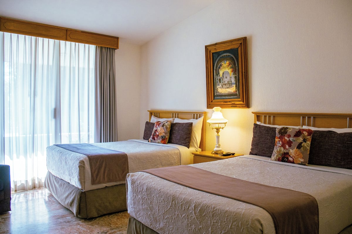 A hotel room with two beds, a painting on the wall, and a window with curtains.