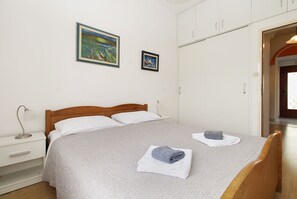 Un lit bien fait, recouvert d’une couverture grise, avec deux oreillers et une serviette pliée posée sur le côté. Deux œuvres d’art encadrées sont accrochées au mur, au-dessus du lit.