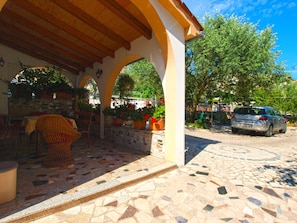 Relax in a serene outdoor space with a wicker chair and table, surrounded by lush greenery and a low stone wall.
