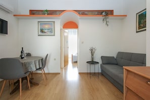A living room with a grey sofa, a dining table with chairs, a small side table with a vase, and a painting on the wall. - Apartment 613/1470 (Istria - Pula), 500m from the beach (Pula)