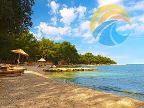 Relax on the beach with sun loungers and a shaded gazebo, surrounded by a natural shoreline and trees.