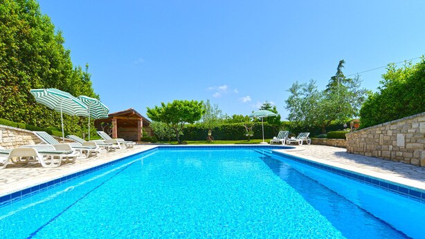 A rectangular swimming pool with clear blue water, surrounded by lounge chairs and umbrellas, set against a backdrop of trees and a stone wall. - Apartment 624/1489 (Istria - Pula), 2500m from the beach (Pula)