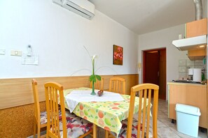 Un coin repas avec une table recouverte d’une nappe à motifs de fruits, entourée de chaises en bois.