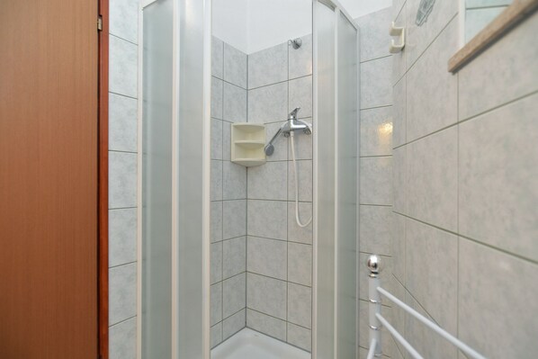 A glass-enclosed shower stall with a handheld showerhead and a wall-mounted faucet.