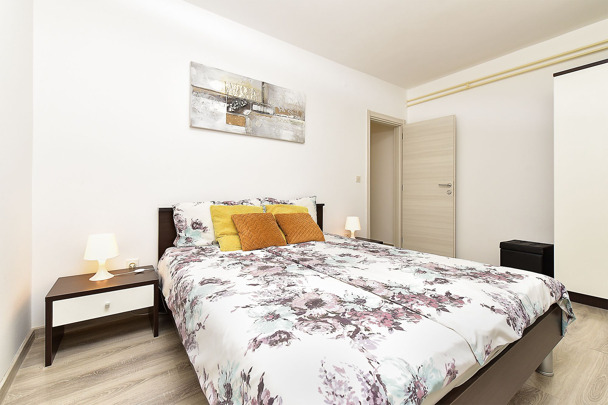 A bedroom with a bed, nightstands, a lamp, a door, and a wall-mounted artwork.