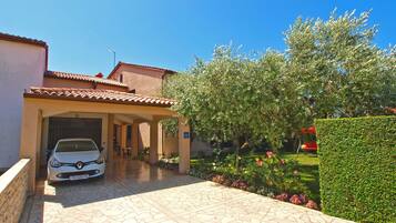 A building with a tiled roof, a car parked in front, and a well-maintained garden with various plants and flowers.