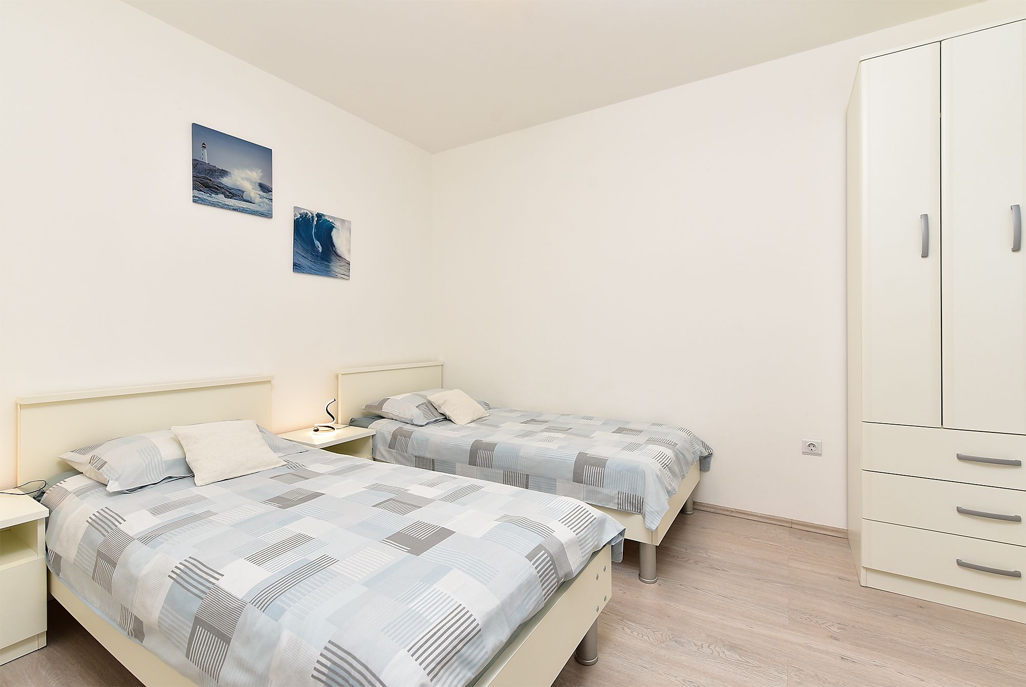 A bedroom with two beds, a wardrobe, and two wall-mounted pictures.