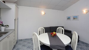 A compact dining area with a round table, white chairs, and a grey cushion. A fruit bowl is on the table, and there are wall-mounted lights. - Apartment 629/26308 (Istria - Rabac), 750m from the beach (Rabac)