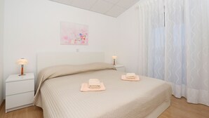 A bedroom with a bed, two bedside tables, a nightstand, a wall-mounted lamp, and a window with curtains. - Apartment 629/26308 (Istria - Rabac), 750m from the beach (Rabac)