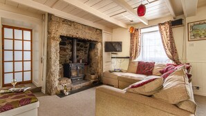 A cozy living room with a stone fireplace, a sofa, a television, and a window with curtains. - Fourways - Four Bedroom Cottage, Sleeps 8 (Townshend)