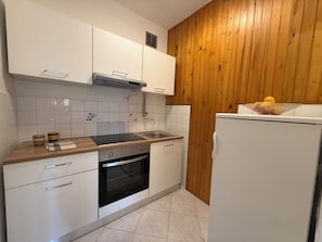 A modern kitchen with white cabinets, a black countertop, a built-in oven, a sink, and wooden paneling on one wall. - Apartment 650/1557 (Istria - Rabac), 100m from the beach (Rabac)