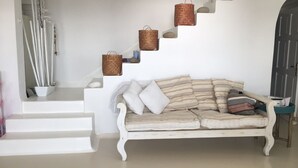 Eine weiße Treppe mit Korbwägelchen auf den Stufen, ein weißes Sofa mit gestreiften Kissen und ein kleiner Tisch mit einem Korb.