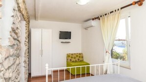 Un dormitorio con pared de piedra, una cama, una silla verde, un televisor y una ventana con cortinas.