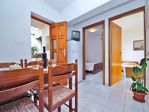 A dining area with a wooden table and chairs, a refrigerator, a television, and a bed in the adjacent room. - Apartment 653/1563 (Istria - Rabac), 500m from the beach (Rabac)