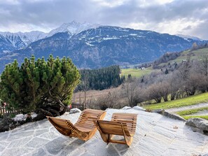 Ein Holzbank- und Tischset auf einer Steinterrasse mit Bergblick.