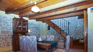 Ein rustikales Interieur mit einem Holzessttisch, gemusterten Stühlen, einer Steinwand und einer Holztreppe.