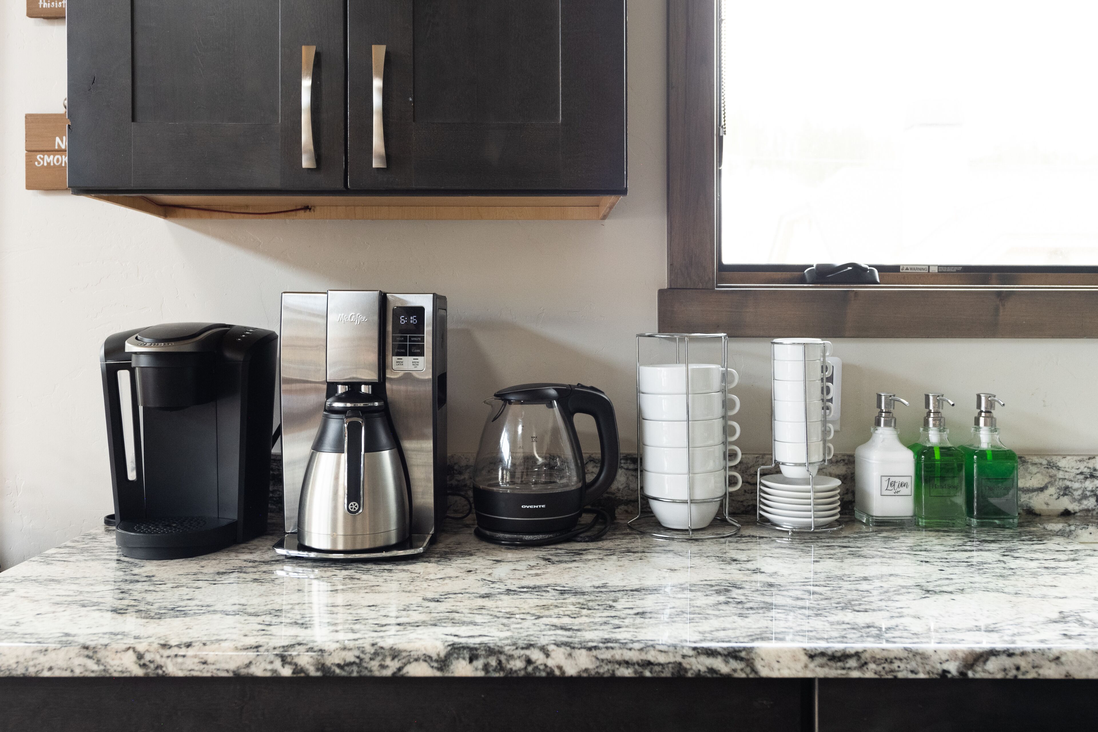 A kitchen counter with a coffee maker, a kettle, and stacked cups.