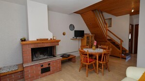 Un salon chaleureux avec une cheminée en briques, une table à manger en bois et un escalier menant à l’étage supérieur.