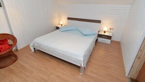 Une chambre à coucher avec un lit, des tables de chevet, une commode, une chaise en osier et un plancher en bois.