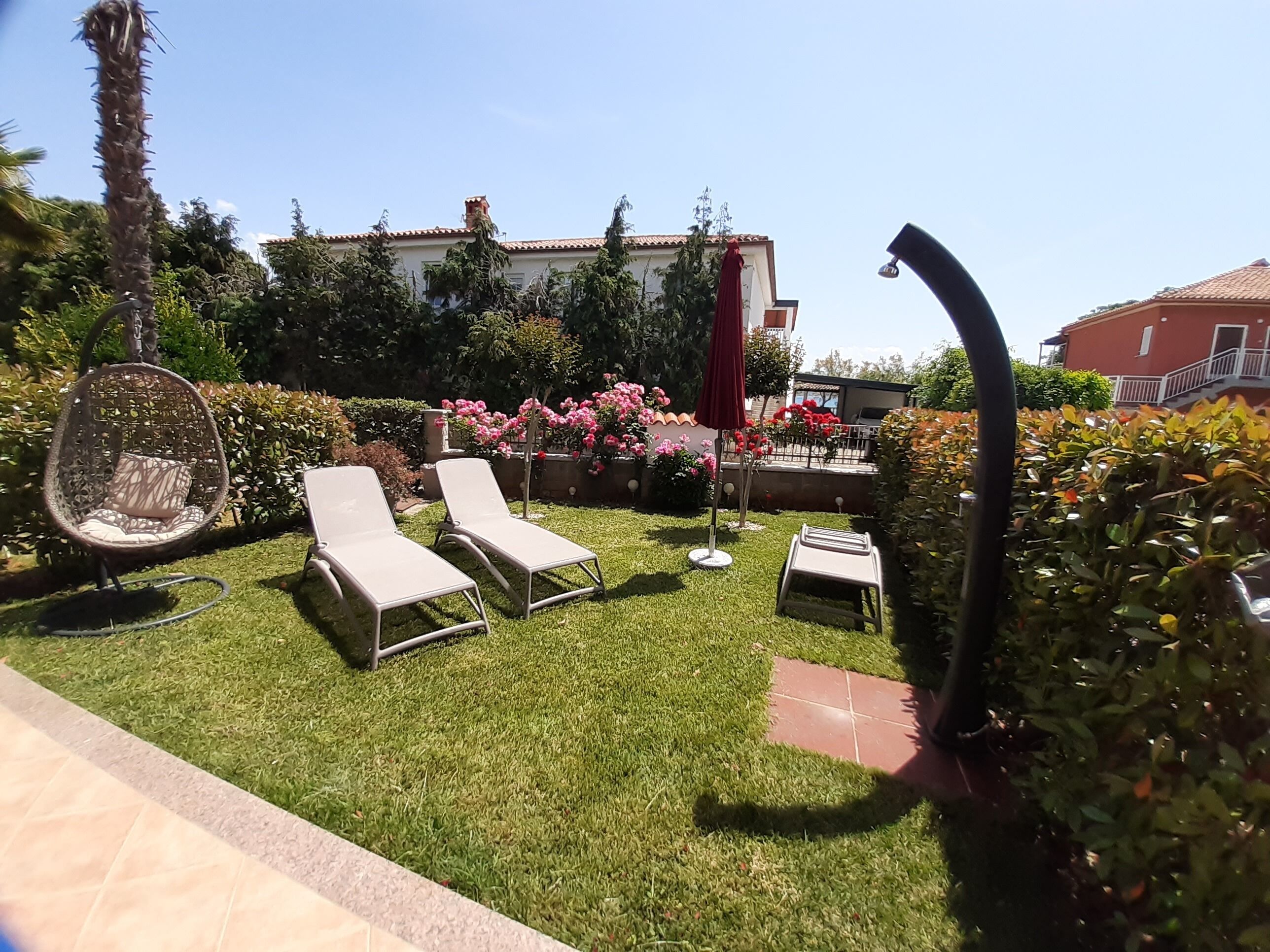 A well-maintained garden with two lounge chairs, a hanging chair, and a small table.