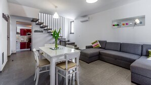 Un salon moderne avec un coin repas, un canapé gris et un escalier menant à la cuisine.