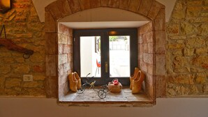 Une pièce aux murs de pierre, avec une fenêtre ornée d’une paire de bottes, d’un vélo et d’un pot.