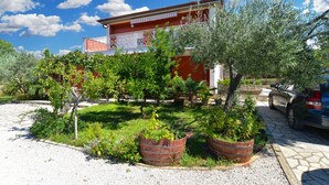 A building with a red facade and a garden with various plants and a car parked in front. - Apartment 684/1615 (Istria - Stinjan), 400m from the beach (Stinjan)