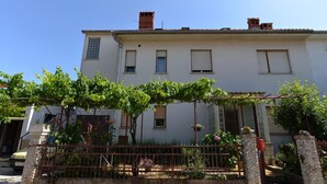 Un bâtiment à deux étages, doté d’une façade blanche, de nombreuses fenêtres et d’un petit jardin agrémenté d’une clôture en métal et de plantes en pot.