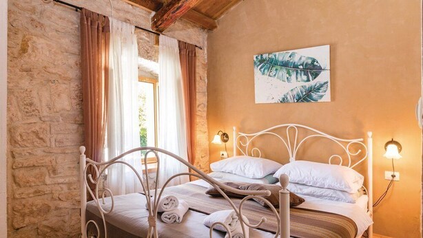 A bedroom with a stone wall, a bed with white metal headboard, and a painting of leaves on the wall. - Villa 704/1643 (Istria - Žminj), 25000m from the beach (Žminj)